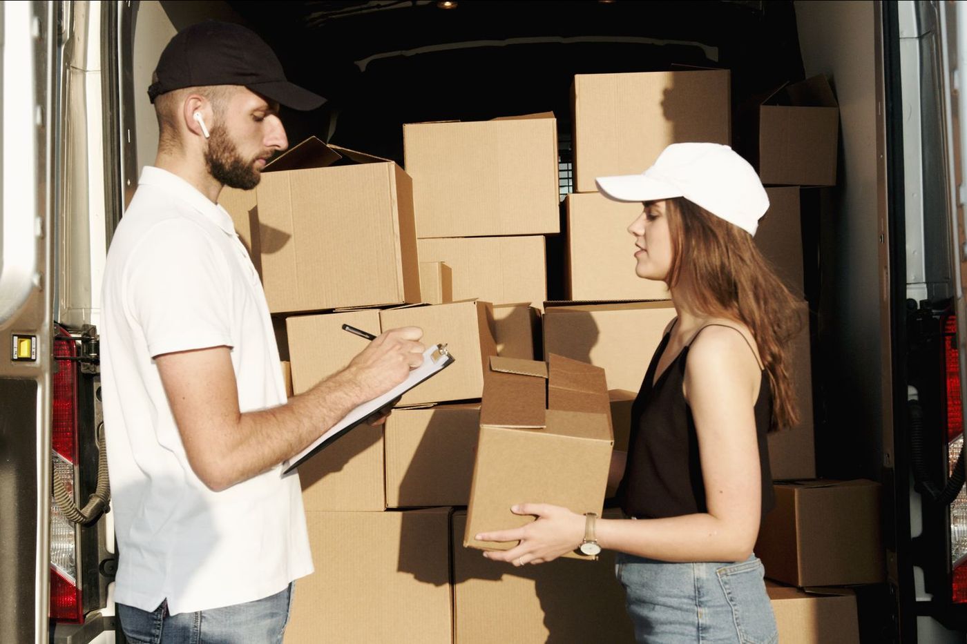 Two movers checking an inventory on a clipboard at the open back of a van loaded with boxes